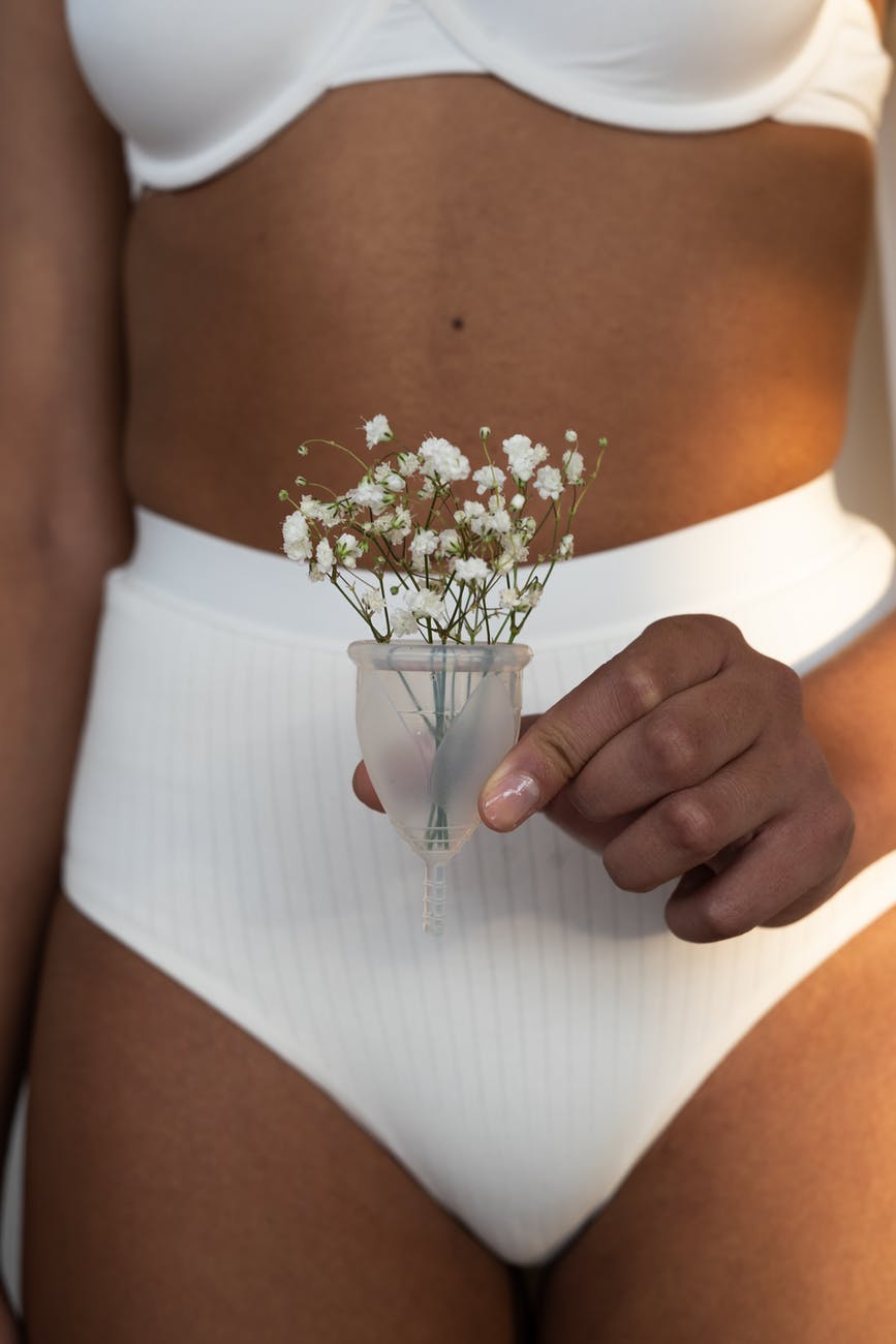 woman in white undergarments holding menstrual cup with flowers